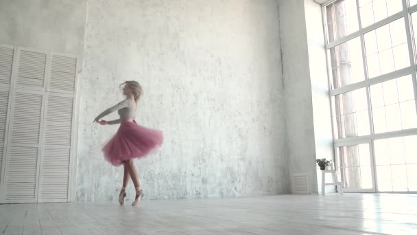 Ballerinan snurrar i en klassisk tutu och pointe skor. En ung ballerina danser på tå mot bakgrund av en stor ljus window.slow rörelse — Stockvideo