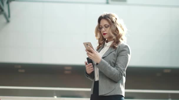 Mujer joven en traje de negocios escribiendo mensaje en el teléfono móvil. retrato de una mujer de negocios en un edificio de oficinas — Vídeos de Stock