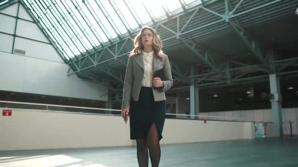 A szürke kabátot és egy szoknya egy fiatal nő végigvezeti a hallban, az irodaház. magabiztos üzletasszony. lassú mozgás — Stock videók