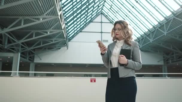 Retrato de una mujer de negocios usando un teléfono inteligente. chica en ropa de negocios en el amplio vestíbulo del centro de negocios — Vídeo de stock