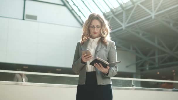 Mujer de negocios en chaqueta gris envía un mensaje desde el teléfono móvil y mira el reloj inteligente — Vídeos de Stock