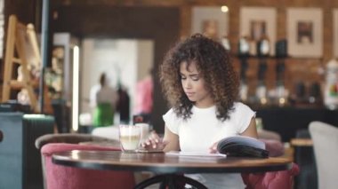 Bir kız çok etnik gruptan oluşan bir görünüme sahip bir kahve evde kahve içer ve cep telefonu üzerinde bir ileti yazdırır