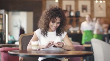 kahve evde bir melez kız portresi. Smartphone'da mesajlaşma ve içtenlikle gülümseyen güzel İspanyol kadın.