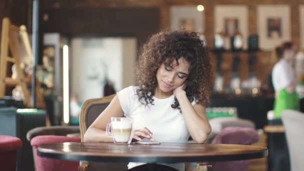 Attrayant hispanique fille en utilisant smartphone et sourit dans un café . — Video