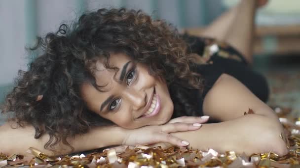 Retrato de uma bela menina de pele escura com confetes e brilhos dourados. conceito do feriado, diversão, comemorar. câmara lenta — Vídeo de Stock