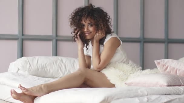Gerade aufwachen hispanisches Mädchen sitzt in der Bettwäsche auf dem Bett und lächelt — Stockvideo