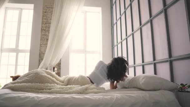 Flickan ligger i sängen, vaknar upp och sträcker sött. bakifrån — Stockvideo