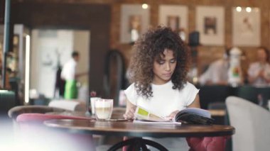 Kız, coffee House menü bakar ve sütlü kahve içer. bir kafede bir masada oturan genç kadın