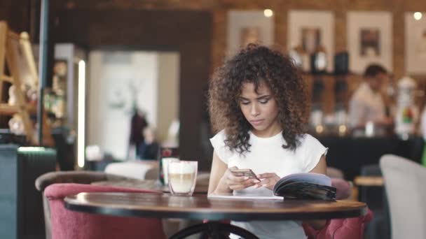 Mädchen im Café. junge hispanische Frau benutzt ein Mobiltelefon, während sie in einem gemütlichen Kaffeehaus sitzt — Stockvideo