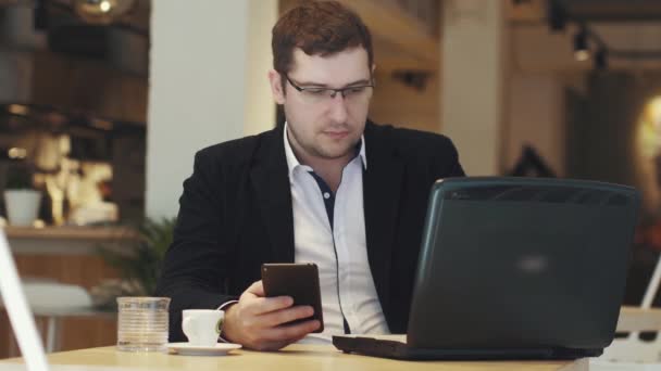 Junger Geschäftsmann sitzt mit Laptop und Smartphone am Tisch im Kaffeehaus — Stockvideo