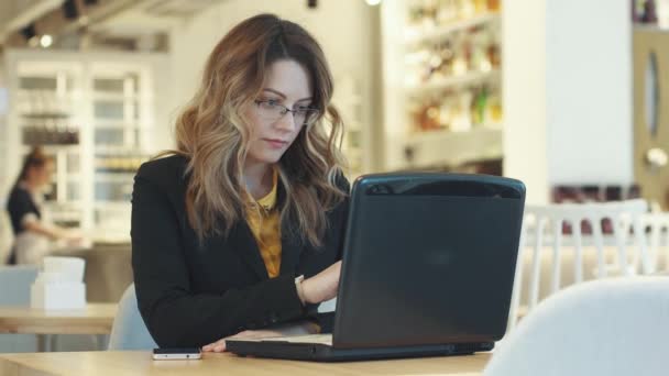 Wanita muda dalam setelan bisnis bekerja pada laptop duduk di kafe. lingkungan kerja informal — Stok Video