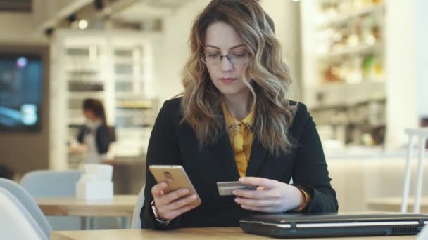 Ένα κορίτσι σε ένα επαγγελματικό κοστούμι διαπράττει μια πληρωμή με πιστωτική κάρτα χρησιμοποιώντας ένα smartphone — Αρχείο Βίντεο
