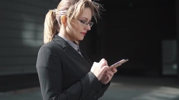 La muchacha en el traje de trabajo envía los mensajes de texto en el teléfono móvil. el viento en tu cabello — Vídeos de Stock