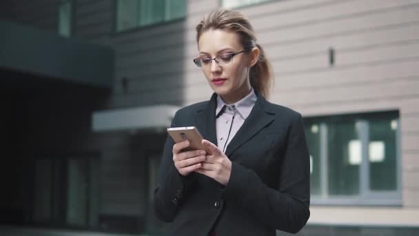 La muchacha en el traje de trabajo envía los mensajes de texto en el teléfono móvil. el viento en tu cabello — Vídeos de Stock