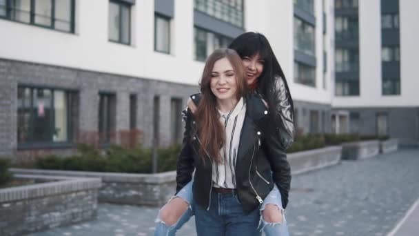 Meninas jovens amigas dando piggyback em férias rindo e andando no calçadão da cidade no verão. morion lento — Vídeo de Stock