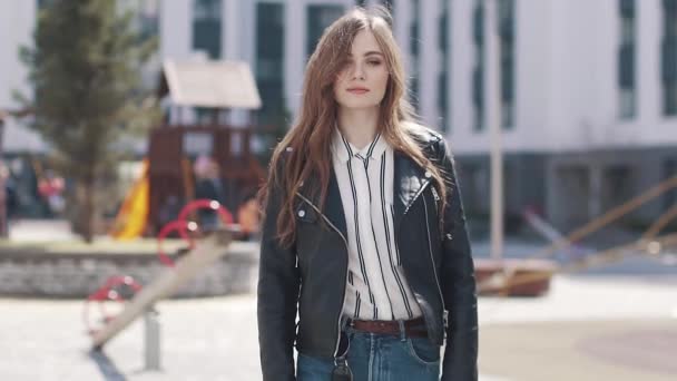 Una giovane ragazza alla moda cammina attraverso la città primaverile al sole. ritratto di una bella giovane donna su uno sfondo di architettura moderna. rallentatore — Video Stock