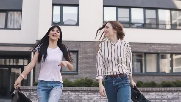 两个朋友在城市里漫步, 享受着美丽的天气。女孩们挥舞着夹克在他们的头上, 笑了起来。慢动作 — 图库视频影像