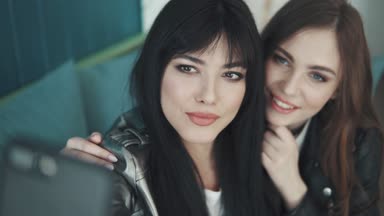 Kız bir kafede otururken hareket eden telefon fotoğraf makinesi üzerinde selfie var. iki çekici kızlar smartphone kamerada fotoğraf çekmek ve aptallık