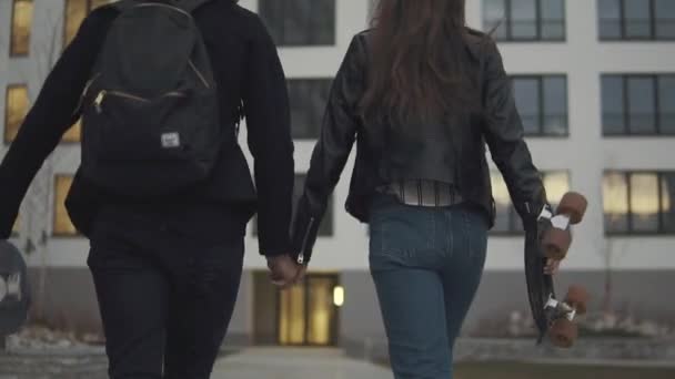 Los jóvenes con patinetas van a dar un paseo nocturno. tipo con su novia ir a patinar en la ciudad de la noche. Vista trasera. cámara lenta — Vídeos de Stock