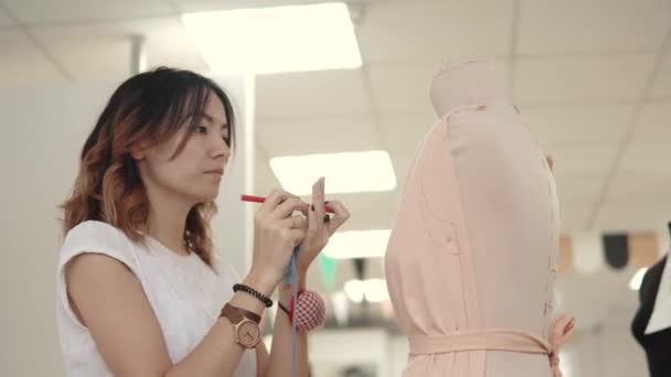 La costurera crea un modelo de ropa en el maniquí. Chica asiática diseñador ropa — Vídeo de stock