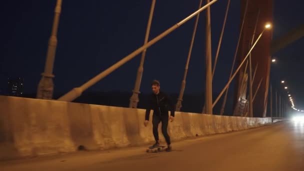 Un joven hipster con barba montando un longboard en una ciudad nocturna — Vídeo de stock