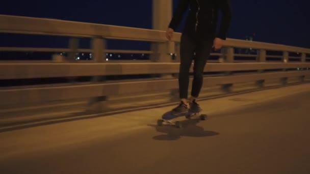 Een jonge kerel skateboarden op een nacht plaats op de rijweg. Hipster manier van reizen — Stockvideo
