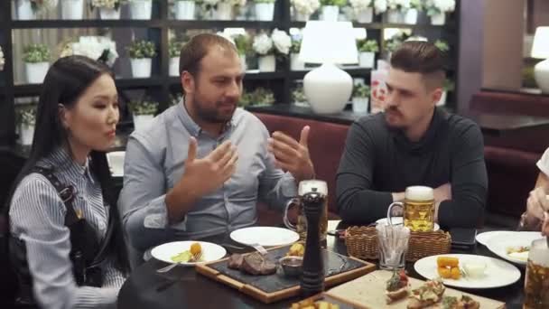 Grupo multiétnico de amigos cenando en un café. una gran empresa divertirse juntos, reír y hablar. hombres clink gafas — Vídeos de Stock