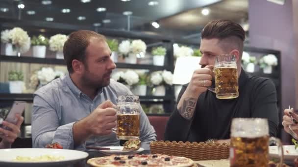 Two friends drink beer and talk in a restaurant. the company gathered for a friendly dinner and have fun together — Stock Video