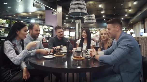 Большая группа друзей разговаривает и веселится вместе сидя за столом в кафе или ресторане — стоковое видео