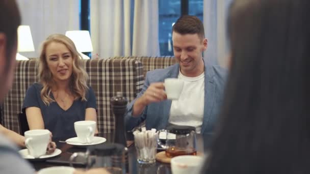 Amigos se ríen y se divierten sentados en una mesa en un restaurante. Una compañía de amigos pasa tiempo juntos y disfruta socializando . — Vídeos de Stock