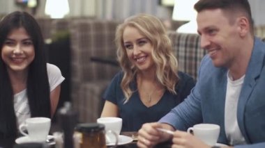 iki kız ve bir genç adam gülüyor ve bir kafe ya da Restoran bir masada otururken gülümseyen