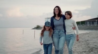 aile gün batımında deniz kıyısında yürür. Genç bir anne çocuklarıile eğleniyor