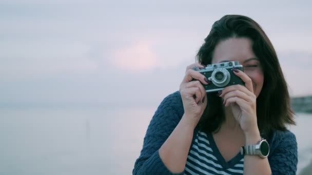 Портрет девушки с ретро-камерой. молодая женщина фотографирует на винтажную камеру у океана — стоковое видео