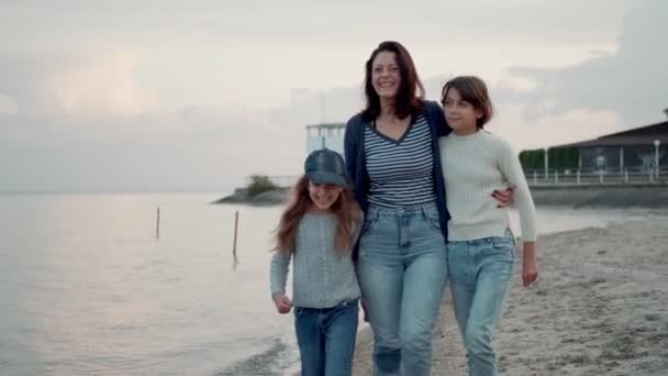 Семейные прогулки вдоль побережья на закате. молодая мать развлекается со своими детьми — стоковое видео
