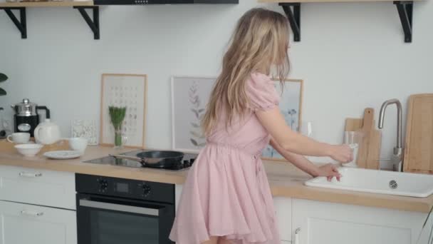 Ragazza versa acqua in un bicchiere dal rubinetto. ritratto di una ragazza carina in cucina — Video Stock