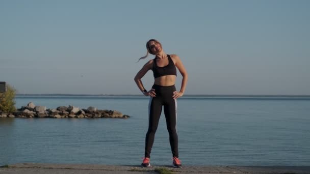 Sportif kız deniz kıyısındaki bir koşu akşamından önce ısınıyor. — Stok video