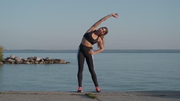 Sportliches Mädchen wärmt sich vor einem Joggingabend am Strand auf — Stockvideo