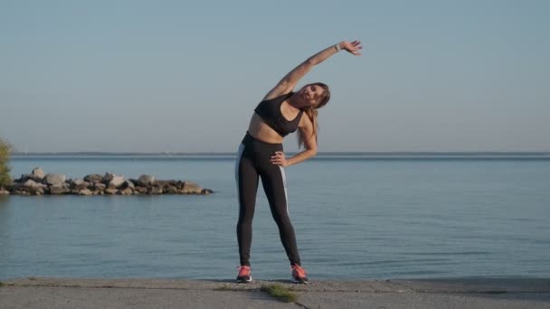 Atletisch meisje is warming-up voor een jogging avond op de kust — Stockvideo