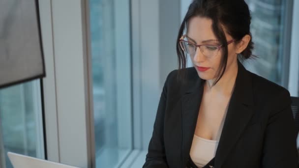 Portrait rapproché d'une jeune femme en costume d'affaires sur le lieu de travail. femme d'affaires travaillant sur ordinateur assis près de la fenêtre dans le bureau — Video