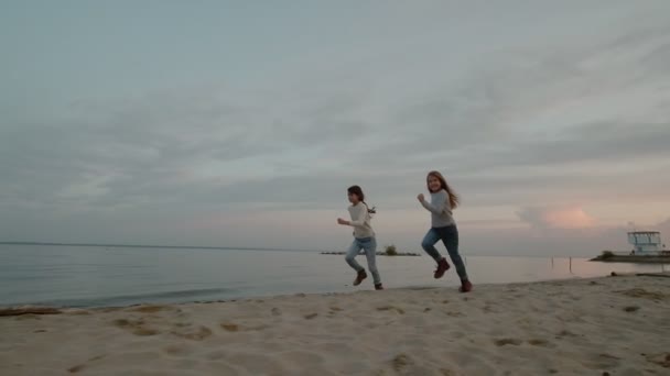 Bezstarostné děti běhají po pobřeží při západu slunce — Stock video