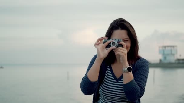 Mujer joven toma fotos en una cámara retro al aire libre . — Vídeos de Stock