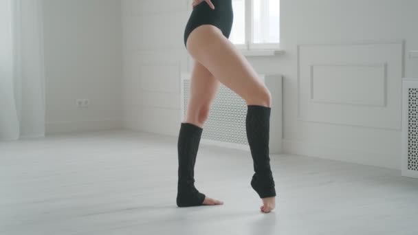 Jovem mulher em um bodysuit preto e leggings aquecendo. dançarina faz alongamento em um estúdio brilhante — Vídeo de Stock