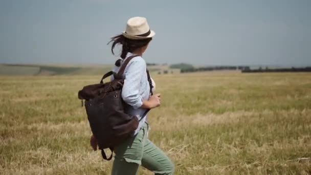 Młoda kobieta podróżnik jest chodzenie z plecakiem po drugiej stronie pola — Wideo stockowe