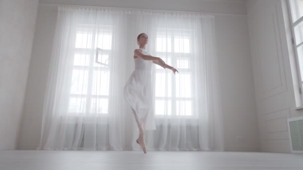 Elegante bailarina está girando de puntillas en un estudio brillante en el fondo de grandes ventanas — Vídeos de Stock