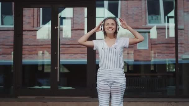 Счастливая девушка в наушниках танцует сумасшедшие на улице — стоковое видео