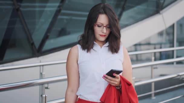 Mujer joven en un traje estricto utiliza un teléfono inteligente — Vídeos de Stock