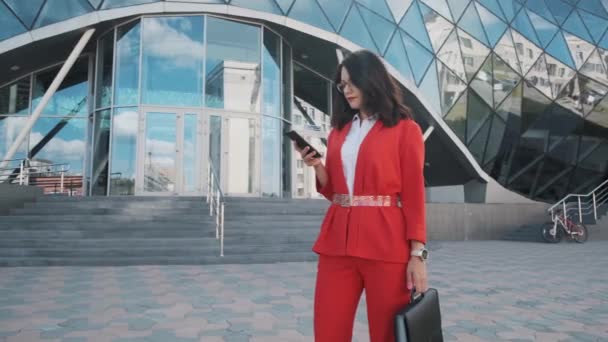 Впевнена бізнес-леді в офіційному костюмі використовує свій мобільний телефон на відкритому повітрі — стокове відео
