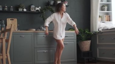Genç bayan mutfakta dans ederek eğleniyor. Kız dikkatsizce dans ediyor ve gülüyor.