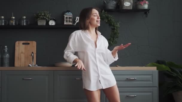 Szczęśliwa dziewczyna ma zabawy i beztroski taniec w domu w godzinach porannych. młoda kobieta zabawny i beztroski taniec w kuchni w białej koszuli — Wideo stockowe