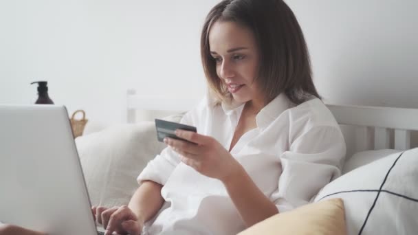 Mulher faz uma compra on-line em casa. menina entra no número do cartão de crédito no laptop — Vídeo de Stock